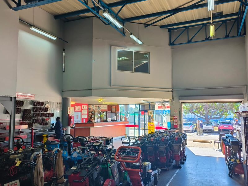 Spacious retail utility and equipment rental area featuring high ceilings with exposed steel trusses, a service counter, and large roller shutter access.