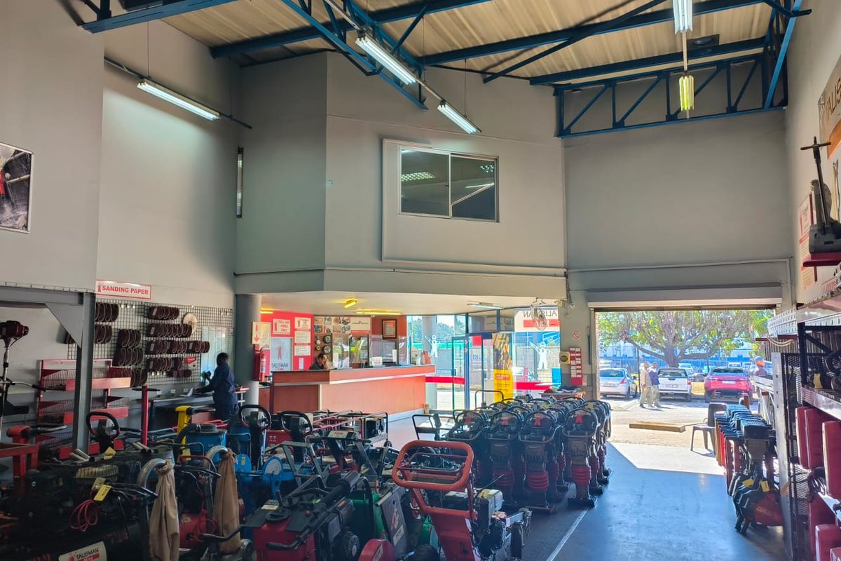 Spacious retail utility and equipment rental area featuring high ceilings with exposed steel trusses, a service counter, and large roller shutter access.