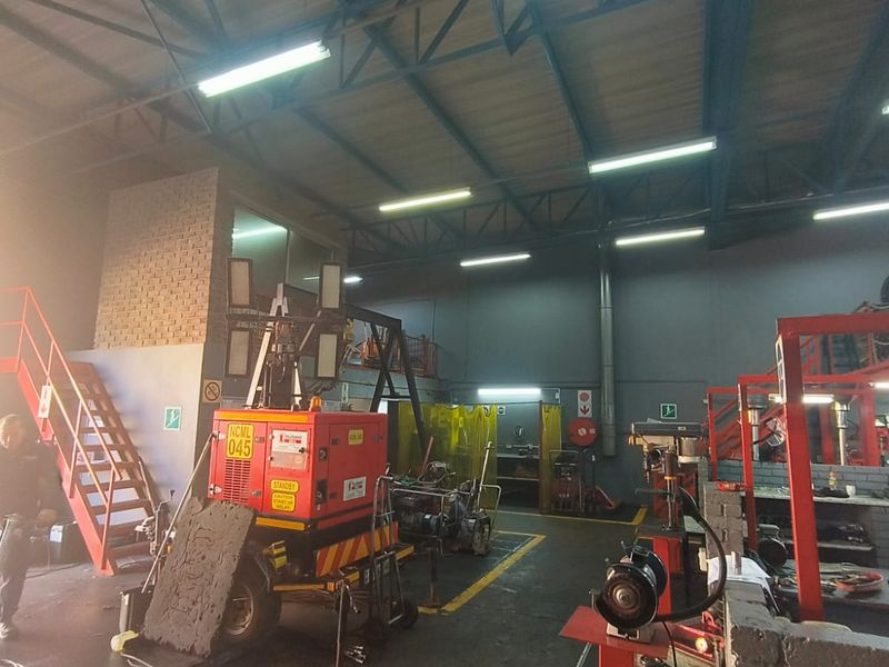 A spacious industrial utility area featuring exposed steel roof trusses, a mezzanine level with metal staircase, and durable concrete flooring.