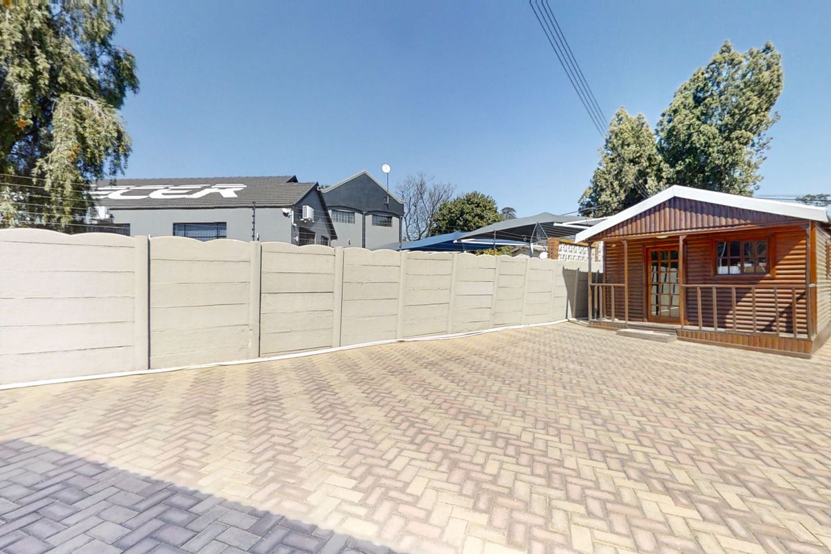 A paved outdoor area featuring a wooden cabin structure, enclosed by a precast concrete boundary wall with electric fencing.