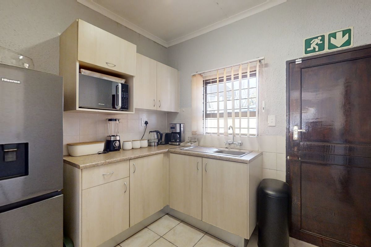 Compact office kitchenette featuring light wood-finish cabinetry, a stainless steel sink, tiled flooring, and a secure exit door with emergency signage.