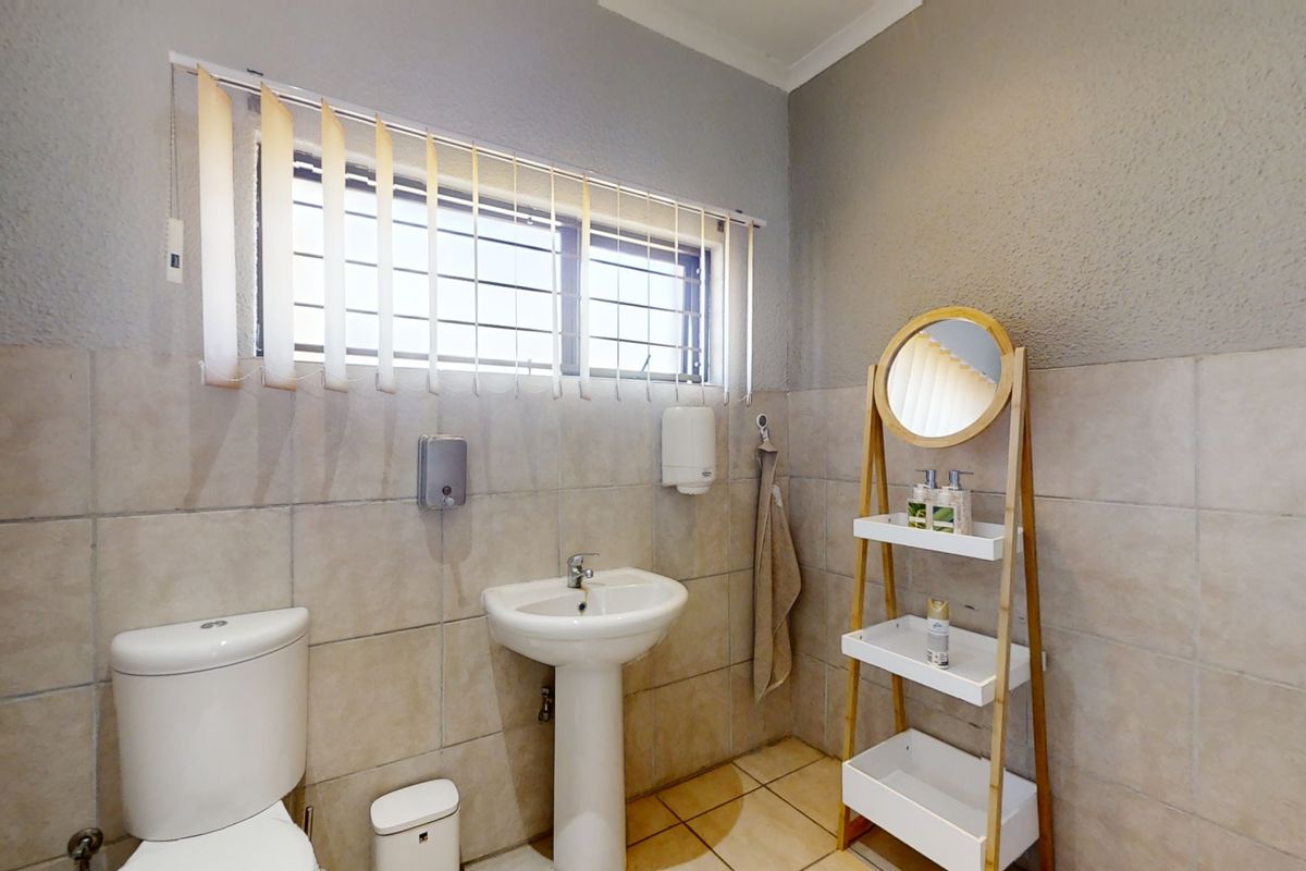 A functional office restroom featuring a pedestal sink, toilet, tiled walls, and a window with vertical blinds.