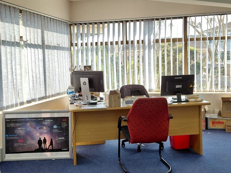 A functional office space featuring large windows with vertical blinds and blue carpet flooring, suitable for a professional work environment.