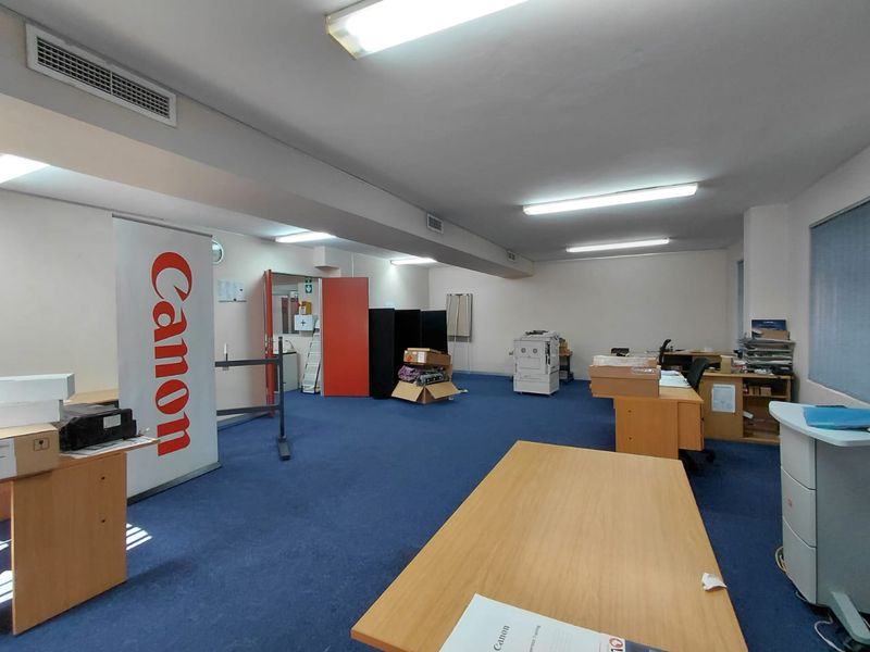 A functional office space featuring blue carpeting, recessed fluorescent lighting, and integrated air conditioning vents, currently utilized as a workspace.