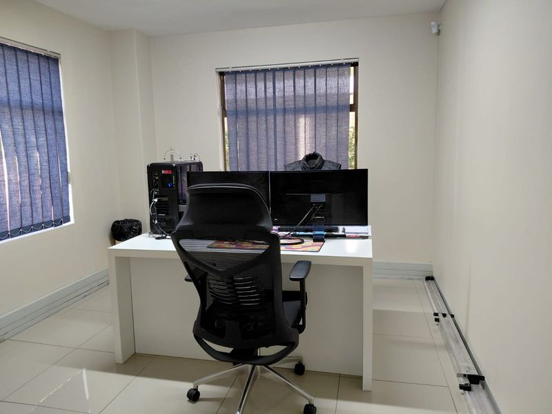 A functional office space featuring tiled flooring, neutral walls, and dual windows with vertical blinds.