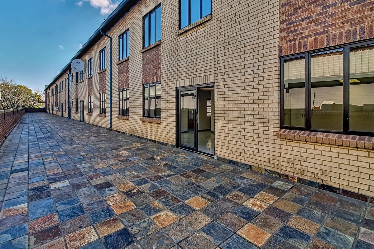 A view of the exterior rear paved walkway and brick facade of the office building, featuring multiple windows and access points.