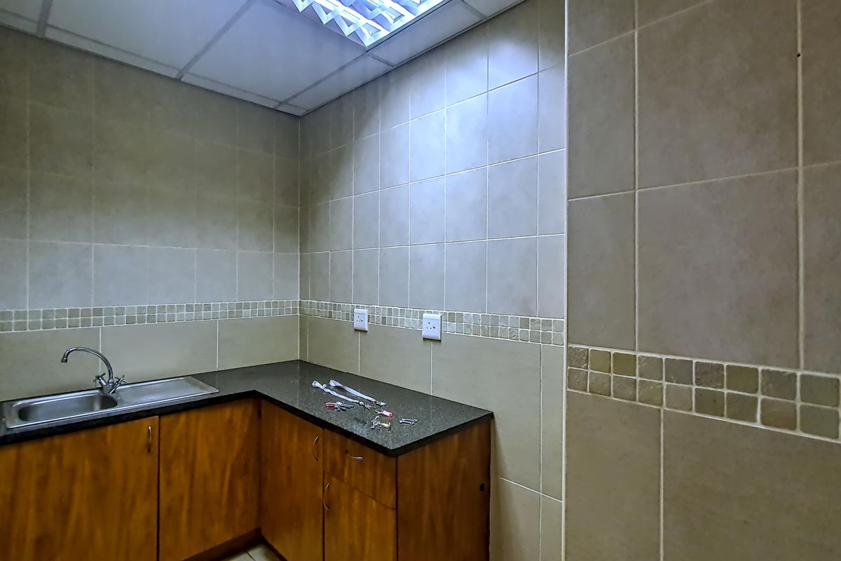 A functional office kitchenette featuring wood-finish cabinetry, a dark granite countertop, a stainless steel sink, and full-height wall tiling.