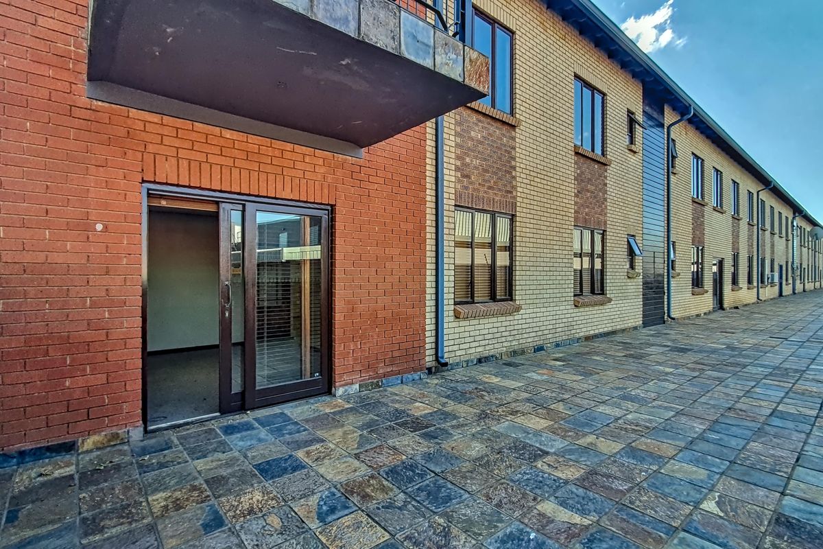 Exterior view of the office building featuring a paved terrace, brick facade, and sliding glass door access to the ground floor office space.