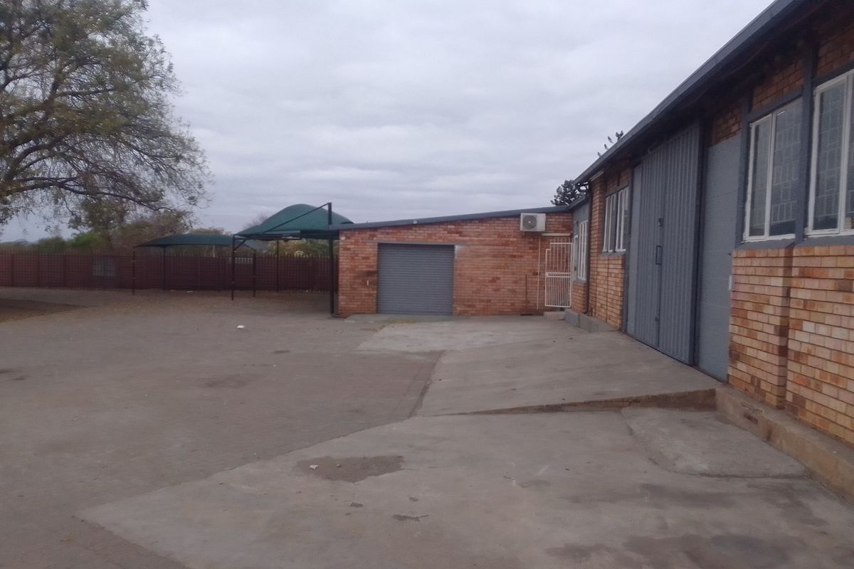 Rear industrial yard featuring a brick building with a roller shutter door, concrete paving, and shade cloth parking structures.