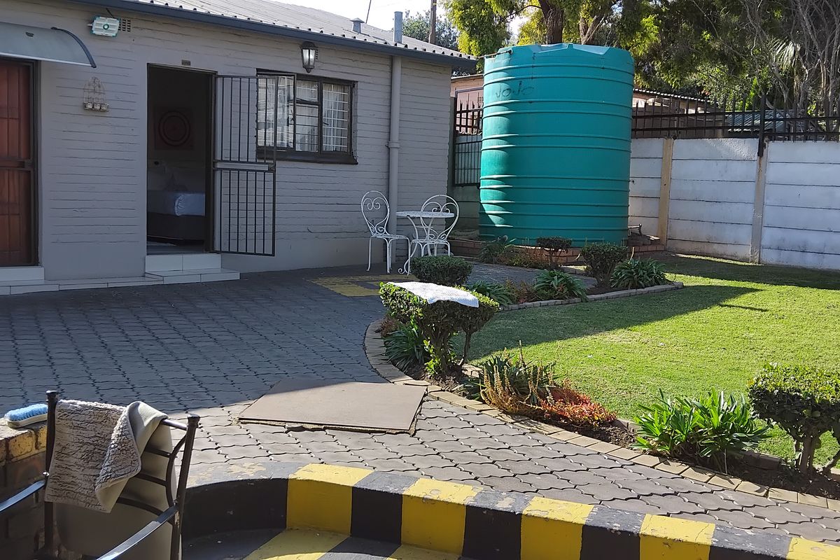 Rear exterior view of the guest house featuring a paved courtyard, lawn area, and a large water storage tank.