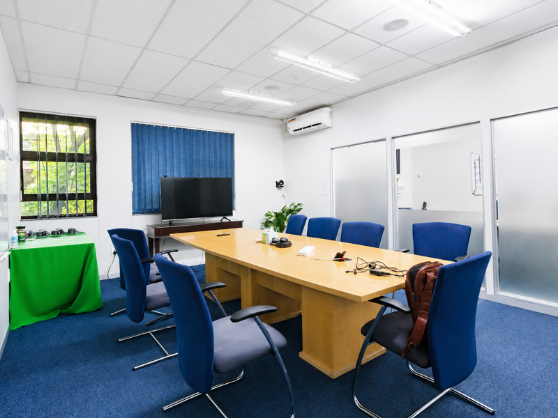 A functional office meeting room featuring a large conference table, glass partitions, suspended ceiling, and split-system air conditioning.