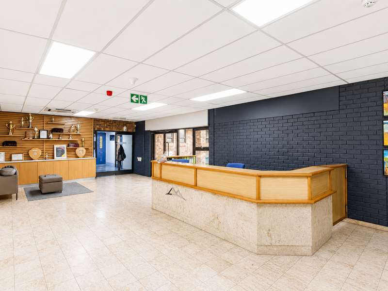 Professional office reception area featuring a custom built-in desk, modern suspended ceiling, and a combination of timber and painted brick wall finishes.