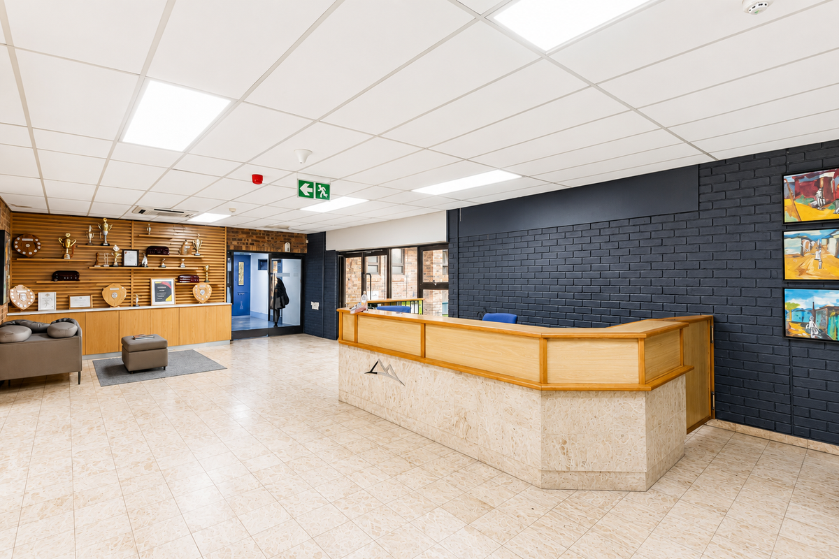 Professional office reception area featuring a custom built-in desk, modern suspended ceiling, and a combination of timber and painted brick wall finishes.