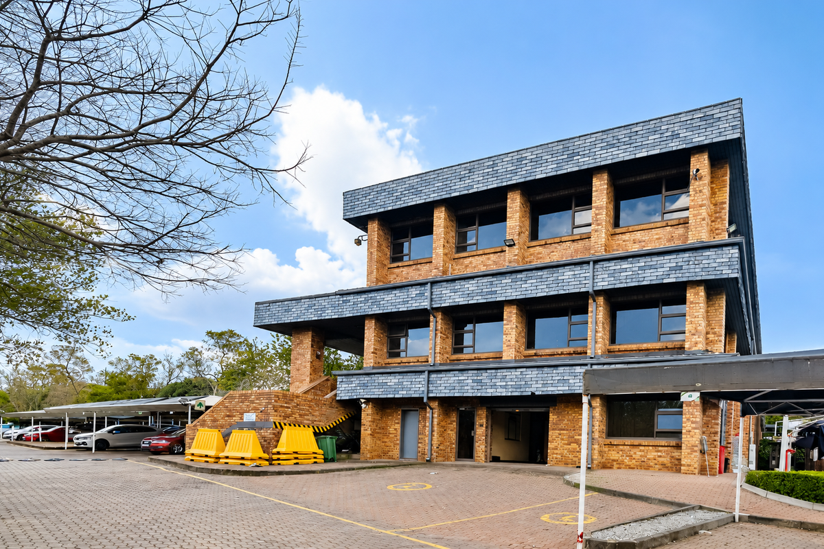 A three-story office building featuring a face brick facade, slate roof detailing, and an adjacent paved parking area with covered bays.