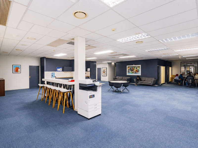 Spacious open-plan office area featuring a central support column, built-in breakfast bar, carpeted flooring, and recessed ceiling lighting.