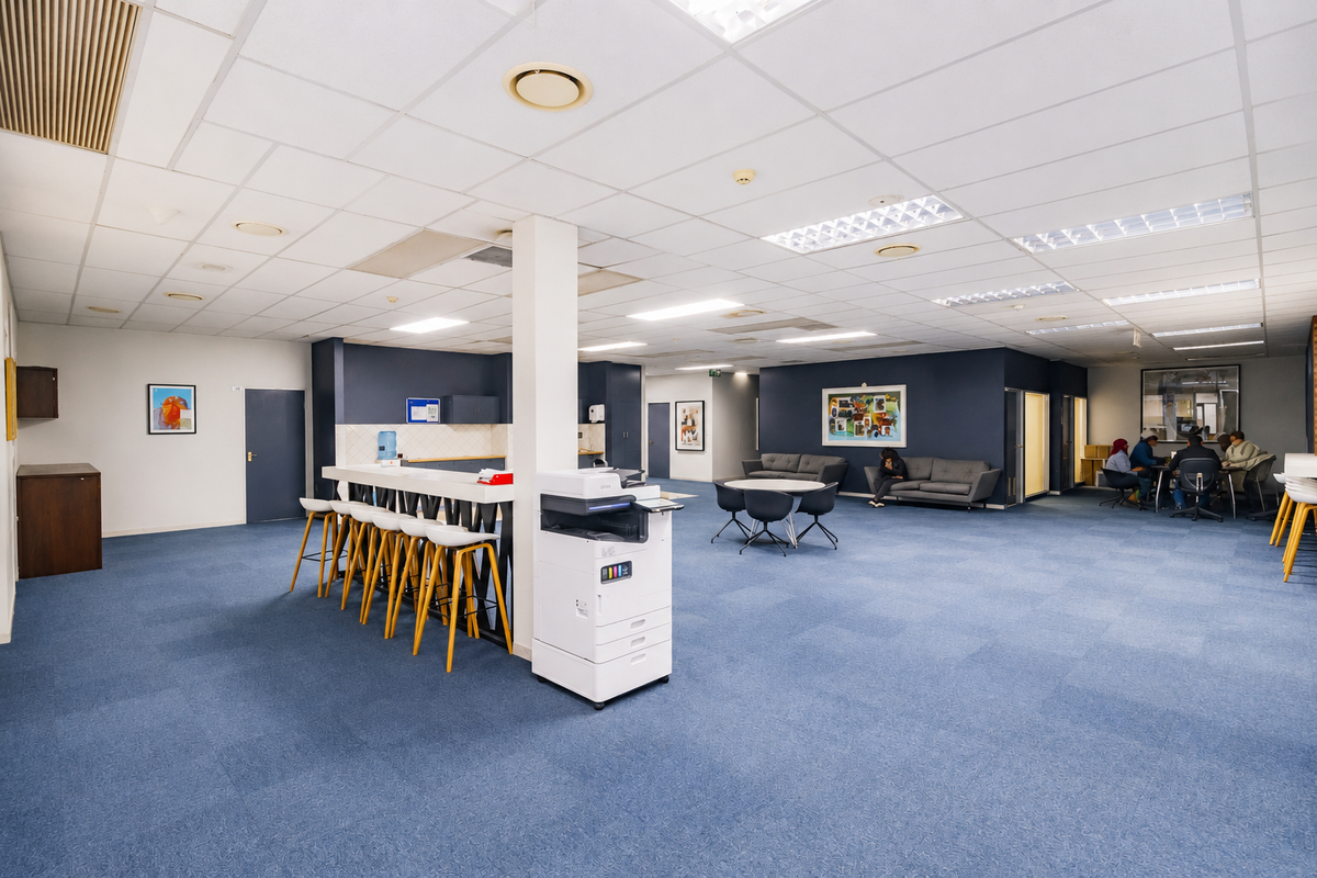 Spacious open-plan office area featuring a central support column, built-in breakfast bar, carpeted flooring, and recessed ceiling lighting.
