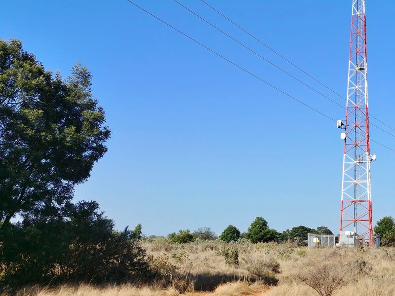 Open farm land featuring a large telecommunications tower and security fencing under a clear blue sky.