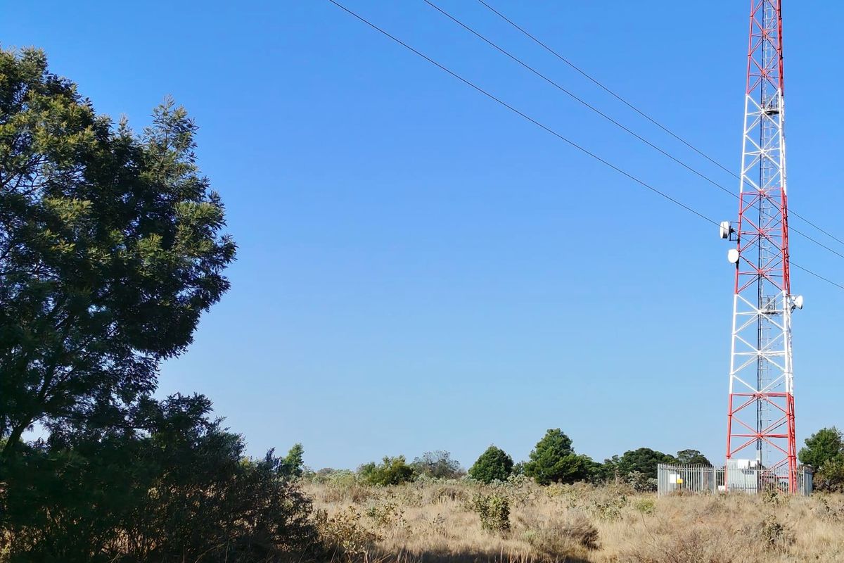 Open farm land featuring a large telecommunications tower and security fencing under a clear blue sky.