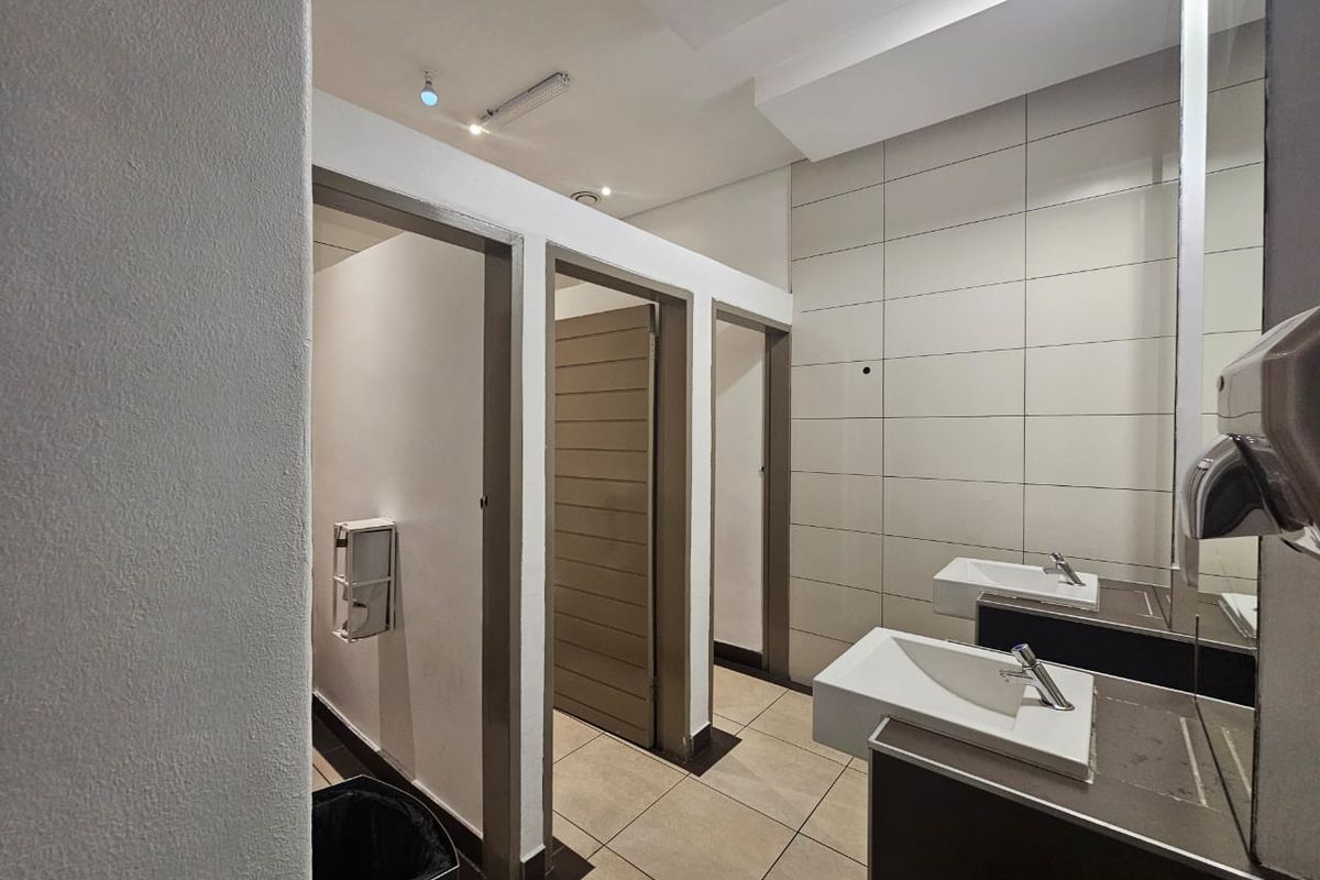 A clean, modern commercial bathroom facility featuring multiple cubicles, wall-mounted basins with chrome mixers, and neutral tiled finishes.