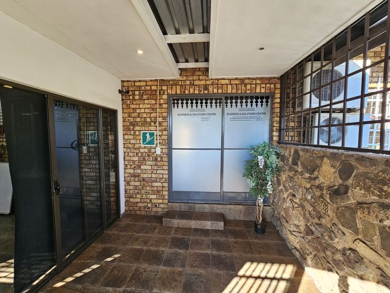 Covered office entrance area featuring tiled flooring, exposed brickwork, stone cladding, and secure sliding glass doors with business signage.