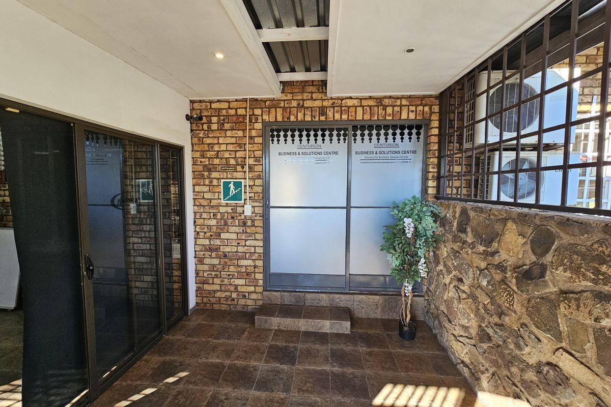 Covered office entrance area featuring tiled flooring, exposed brickwork, stone cladding, and secure sliding glass doors with business signage.