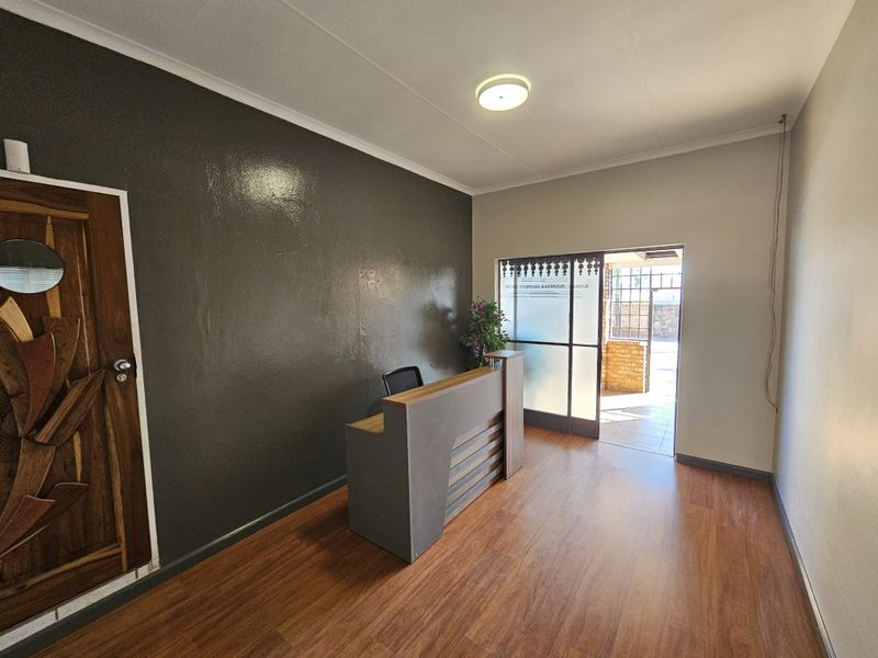 A professional office entry area featuring laminate flooring, a built-in reception desk, and a glass sliding door leading to an outdoor space.