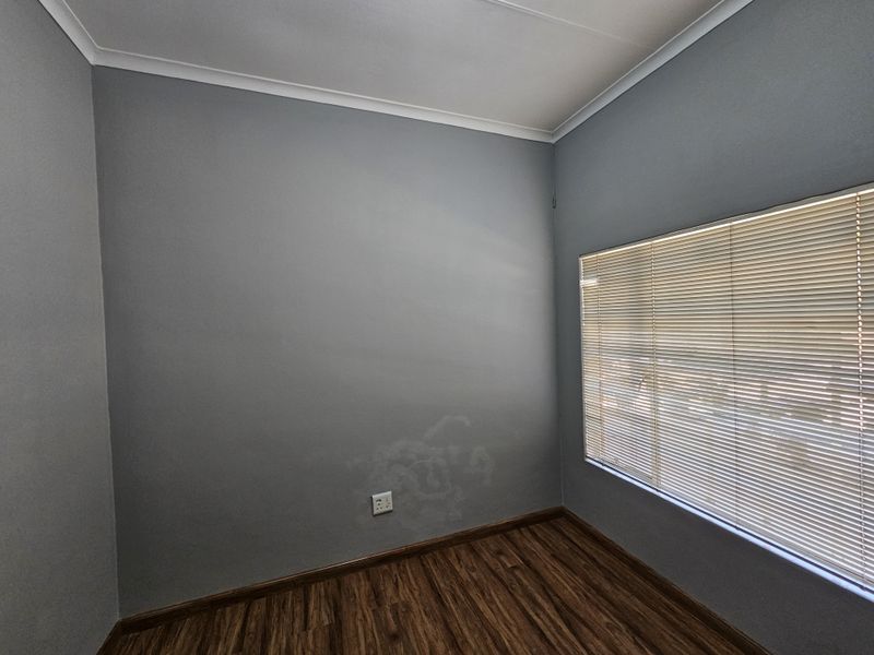 A vacant office space featuring laminate flooring, neutral grey walls, and fitted venetian blinds, providing a clean and functional workspace.