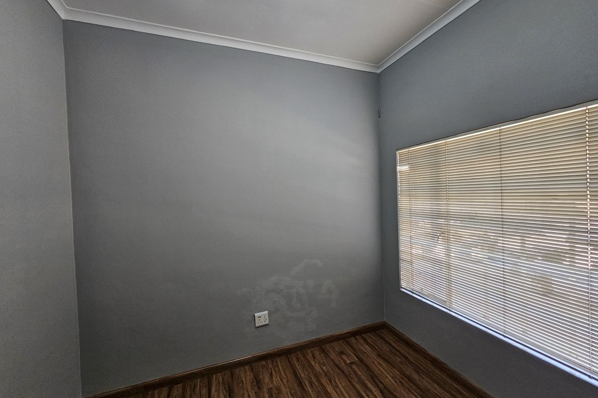 A vacant office space featuring laminate flooring, neutral grey walls, and fitted venetian blinds, providing a clean and functional workspace.