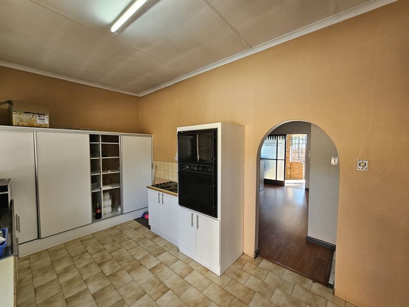 A functional kitchen area featuring built-in oven and hob, fitted cabinetry, and tiled flooring, with an arched doorway leading to an adjacent room.