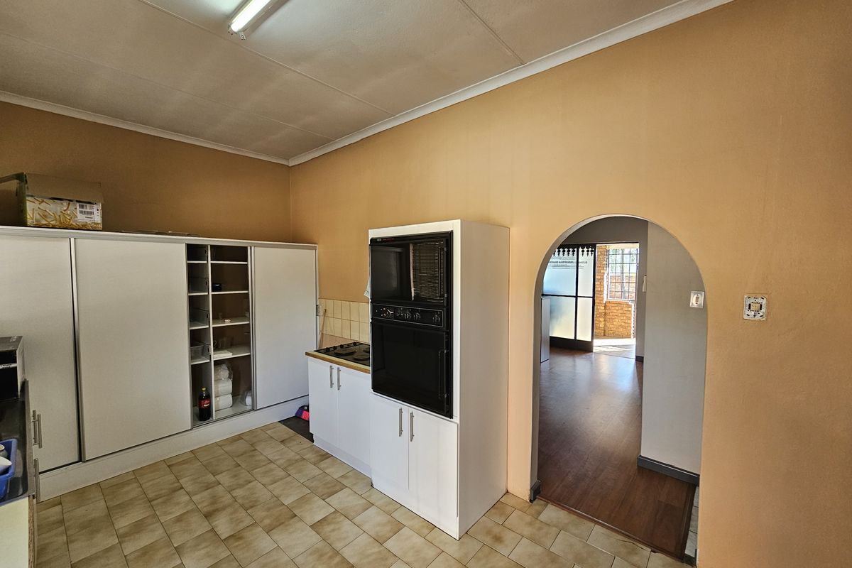 A functional kitchen area featuring built-in oven and hob, fitted cabinetry, and tiled flooring, with an arched doorway leading to an adjacent room.