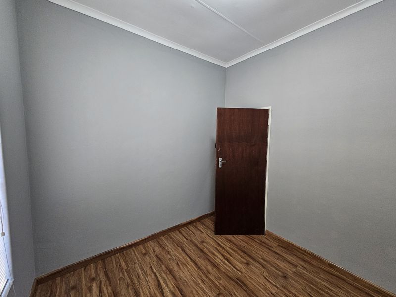 A clean, empty office space featuring modern grey walls, wood-look laminate flooring, and classic coving detail.