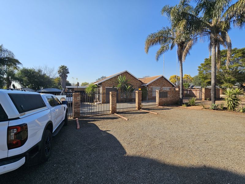Front exterior view of the office property featuring a brick facade, tiled roof, and a secure gated entrance with a gravel parking area.