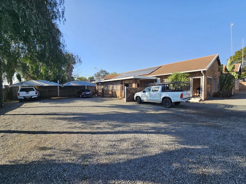 Front exterior view of the office property featuring a large gravel parking area, shade cloth carports, and solar panels installed on the tiled roof.