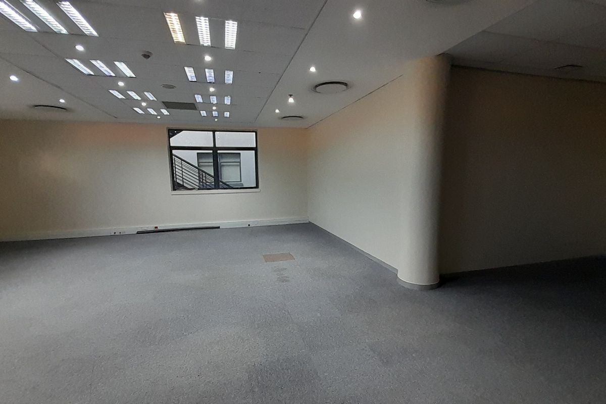 A spacious, empty office area featuring a suspended ceiling with integrated lighting, carpeted flooring, and a prominent structural column.