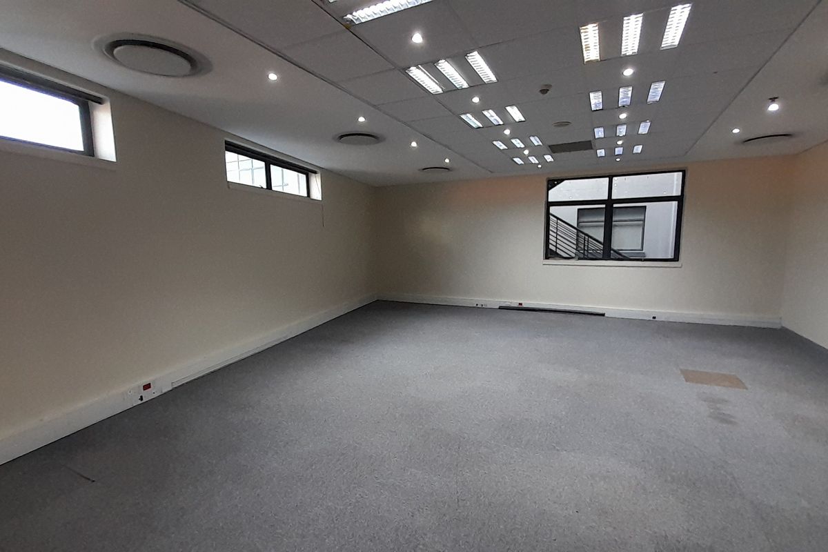 A spacious, empty office area featuring a suspended ceiling with recessed lighting, air conditioning vents, and carpeted flooring.