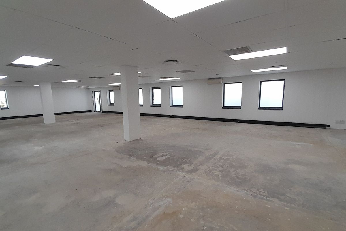 A large, open-plan office space featuring a suspended ceiling, recessed lighting, and structural columns, currently awaiting flooring installation and final finishes.