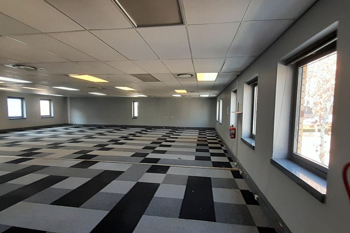 A spacious, open-plan office area featuring a suspended ceiling, recessed lighting, and patterned carpet tiles, offering a versatile workspace with natural light.