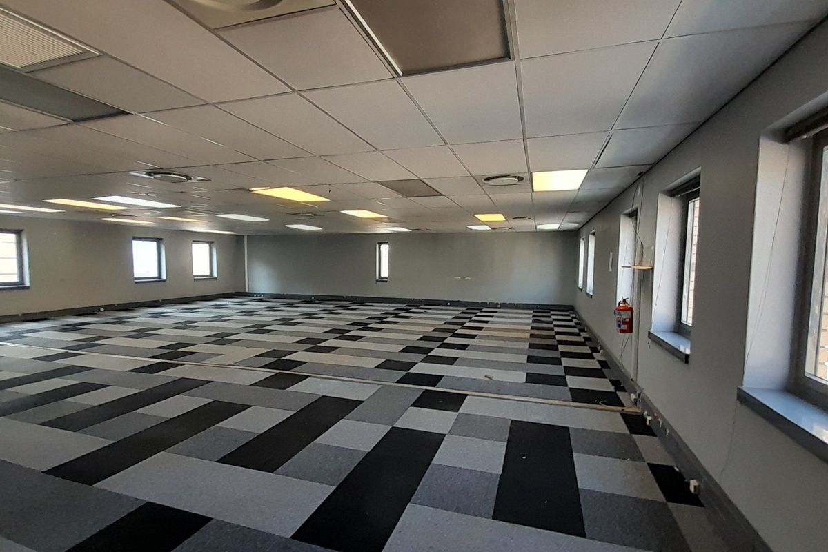 A large, open-plan office space featuring a suspended ceiling, recessed lighting, and patterned carpet tiles, offering a versatile layout for various business configurations.