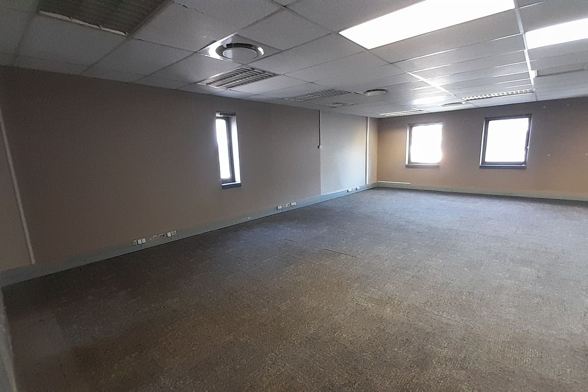 A spacious, empty office area featuring a suspended ceiling with recessed lighting, carpeted flooring, and multiple wall-mounted electrical and data connection points.
