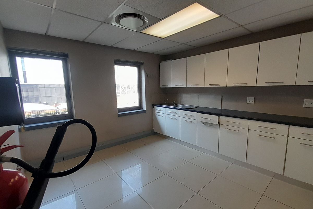 A functional office kitchenette featuring white built-in cabinetry, a dark laminate countertop, stainless steel sink, and tiled flooring.