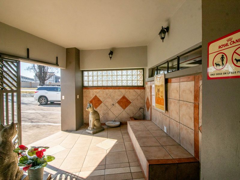 A covered outdoor patio area featuring tiled flooring, a built-in tiled bench, and glass block windows, providing a functional waiting or transition space.