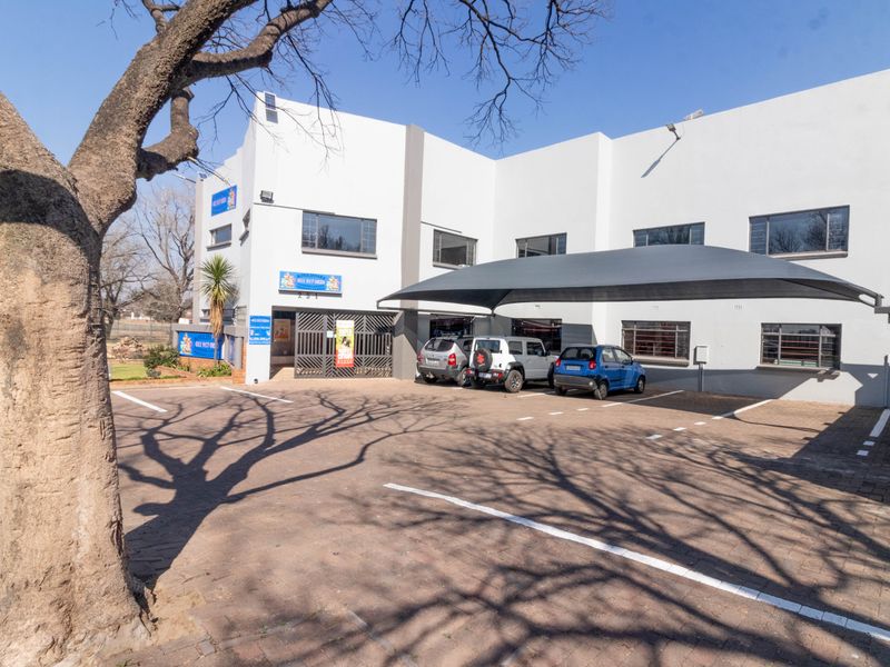 Front exterior view of the office building featuring a paved parking area, shade cloth carport, and secure entrance access.