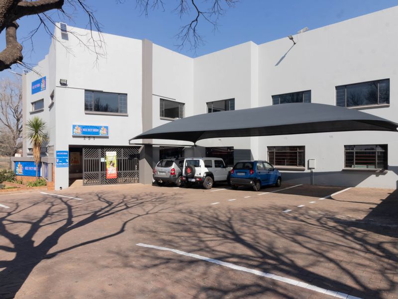 Front exterior view of the office building featuring a paved parking area, shade sail carport, and secure gated entrance.