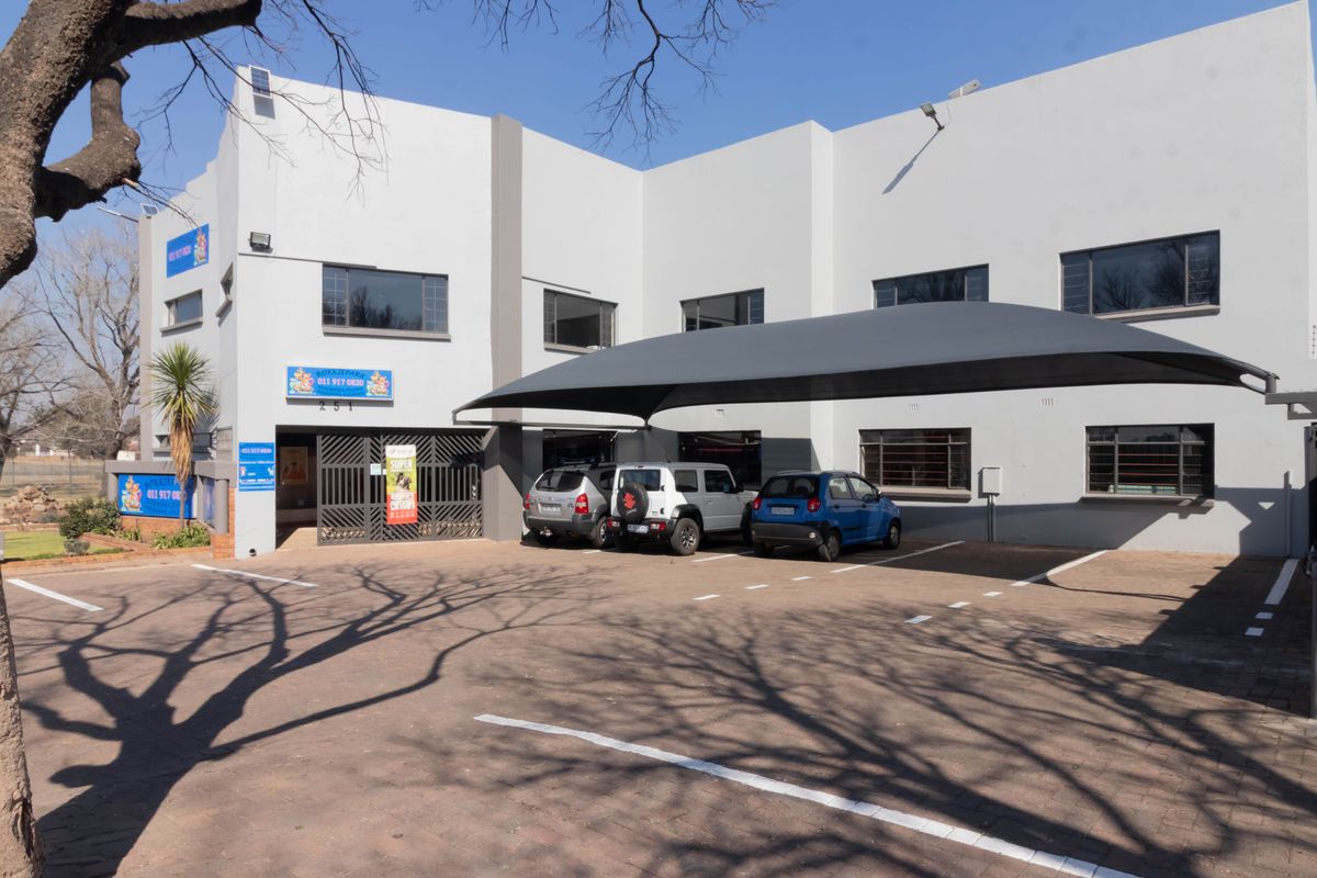 Front exterior view of the office building featuring a paved parking area, shade sail carport, and secure gated entrance.