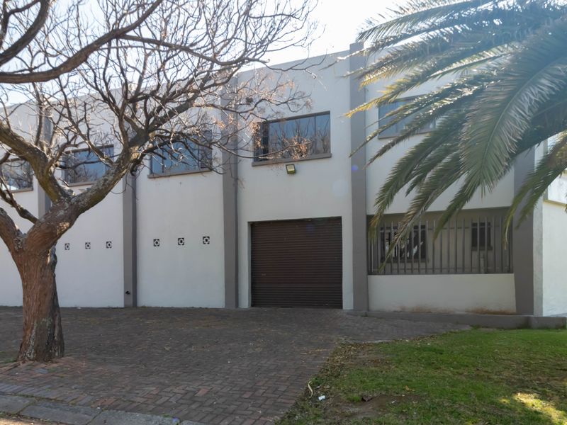 Front exterior view of a commercial office building featuring a paved driveway, roller shutter access, and security-fitted windows.