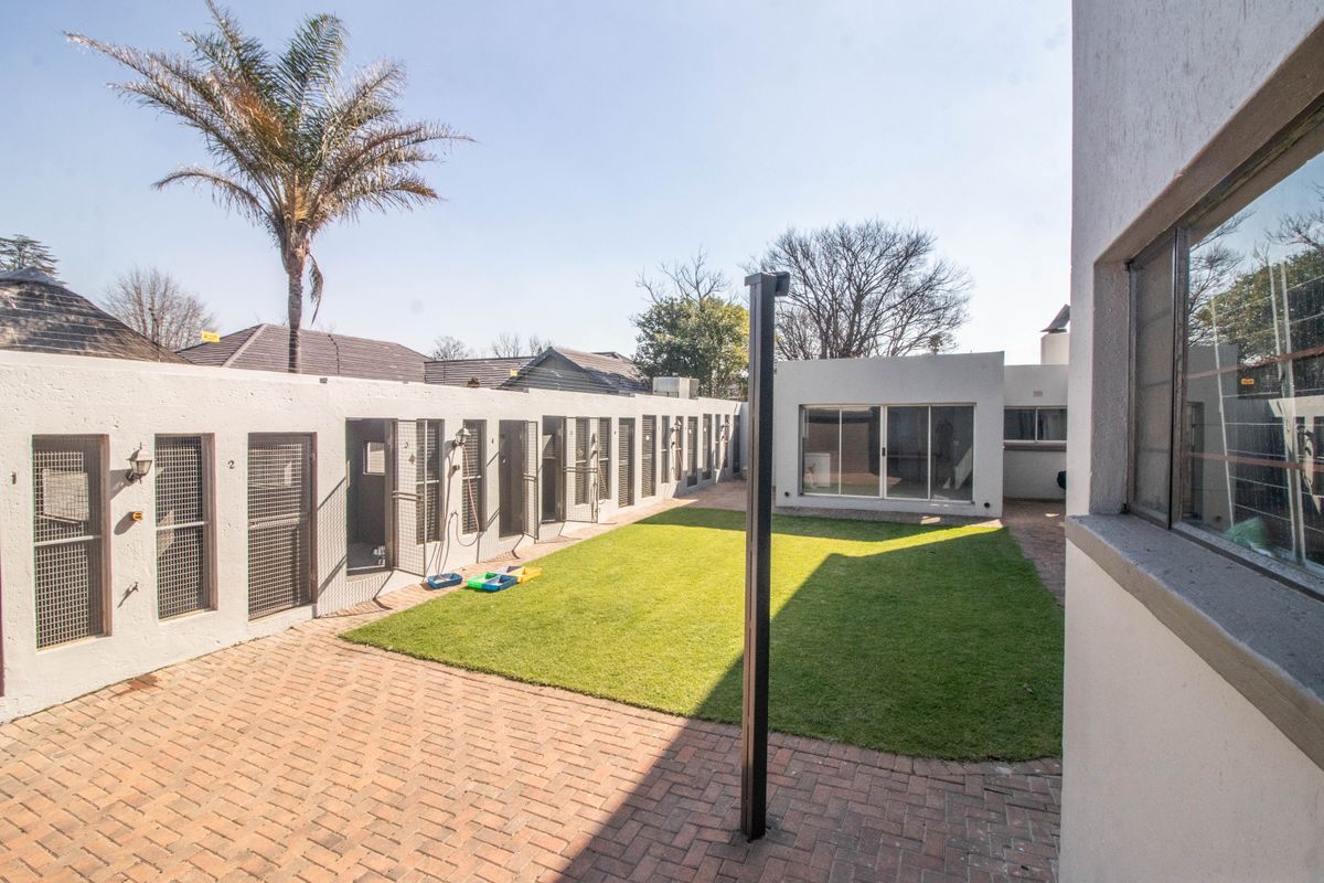 Rear courtyard area featuring brick paving, a central lawn, and a row of secure individual access units with metal gates.