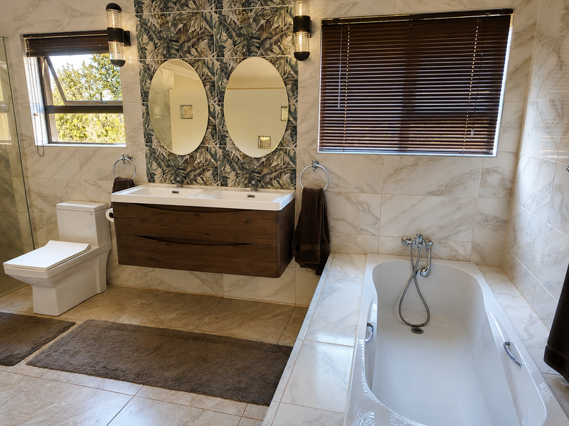 Modern bathroom featuring a double vanity with wall-mounted cabinetry, a built-in bathtub, tiled finishes, and large windows with venetian blinds.