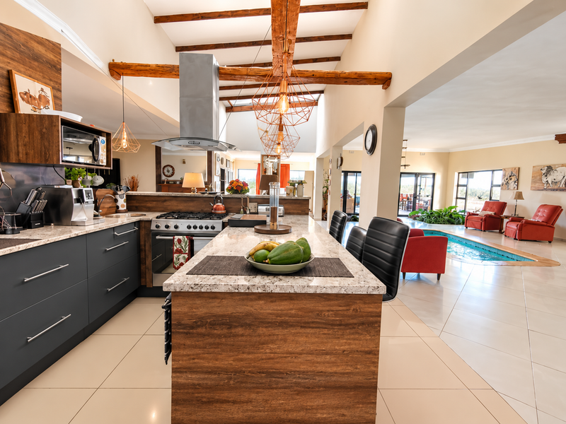 Spacious open-plan kitchen featuring a large island, granite countertops, and exposed timber beams, seamlessly flowing into a living area with an indoor pool.