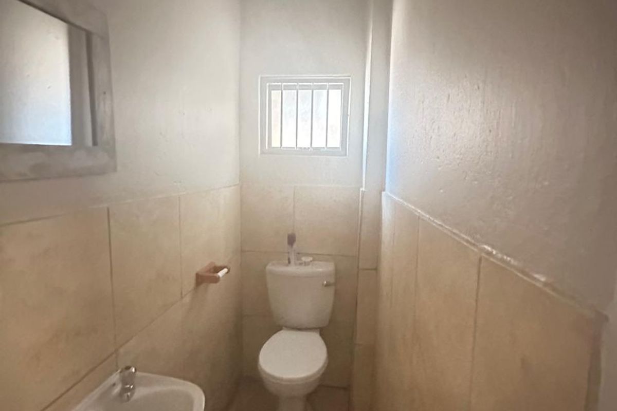 A compact guest bathroom featuring a wall-mounted basin, a standard toilet, and neutral wall tiling.