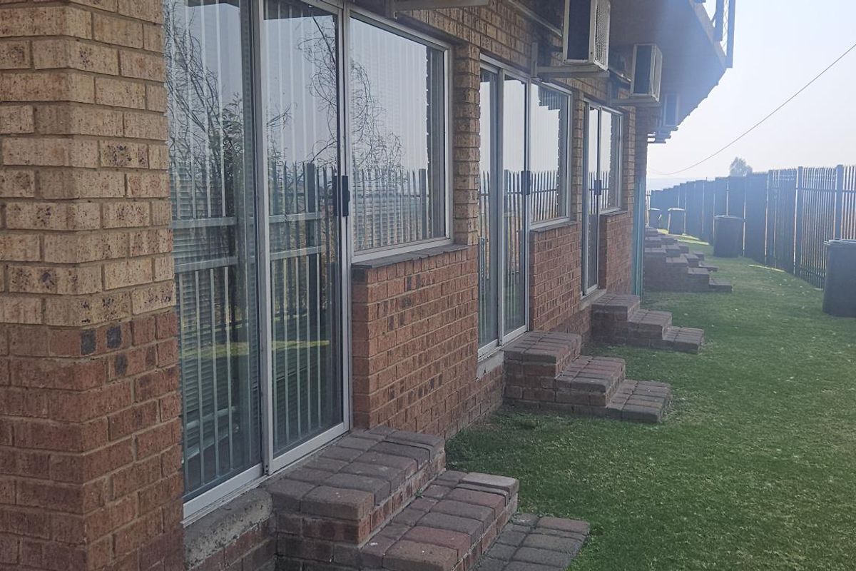 Exterior view of a commercial building featuring face-brick facade, sliding glass doors with security bars, and individual paved step access to a lawn area.